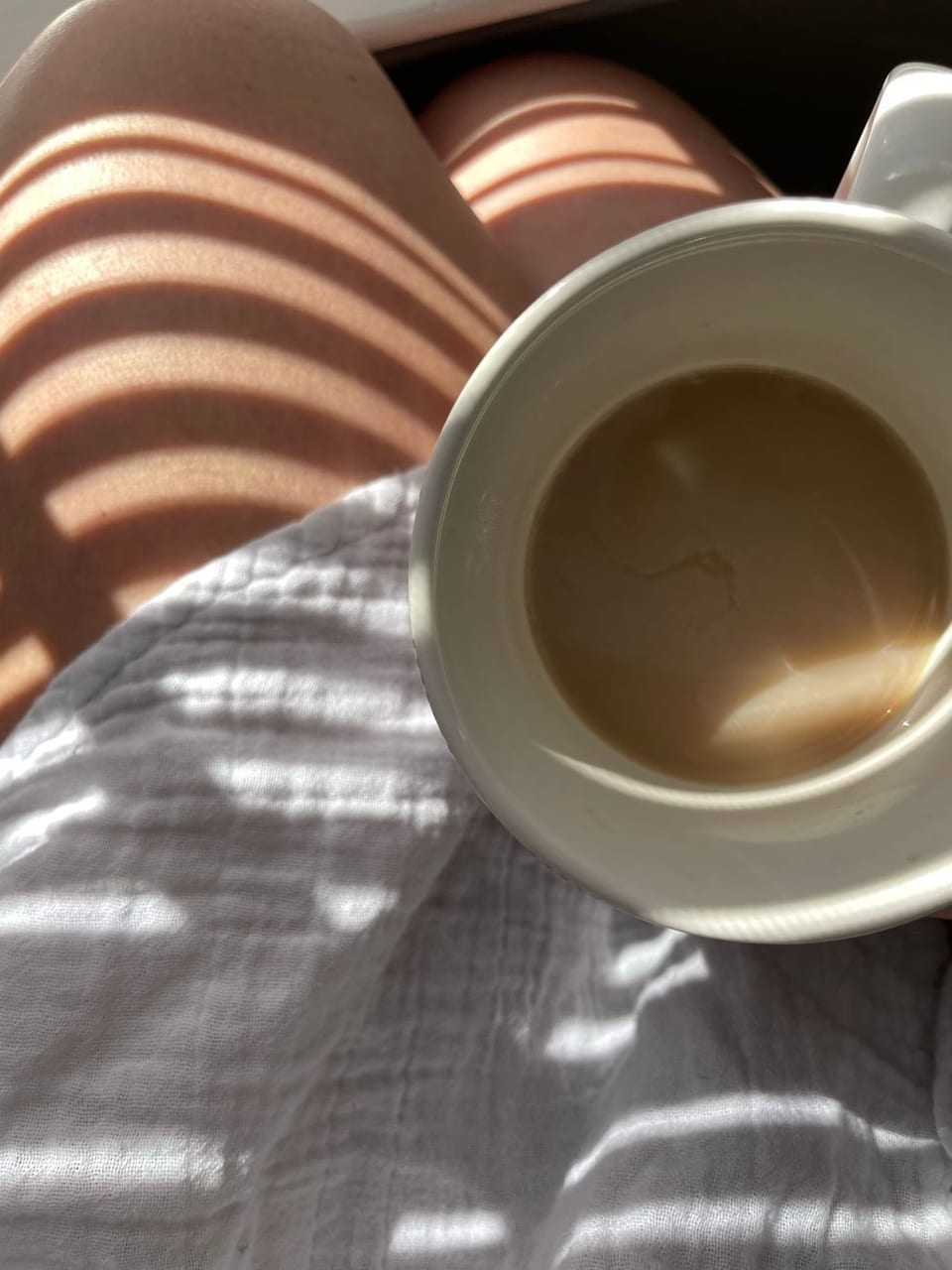 Under a blanket with a warm cup, sun on the sheets