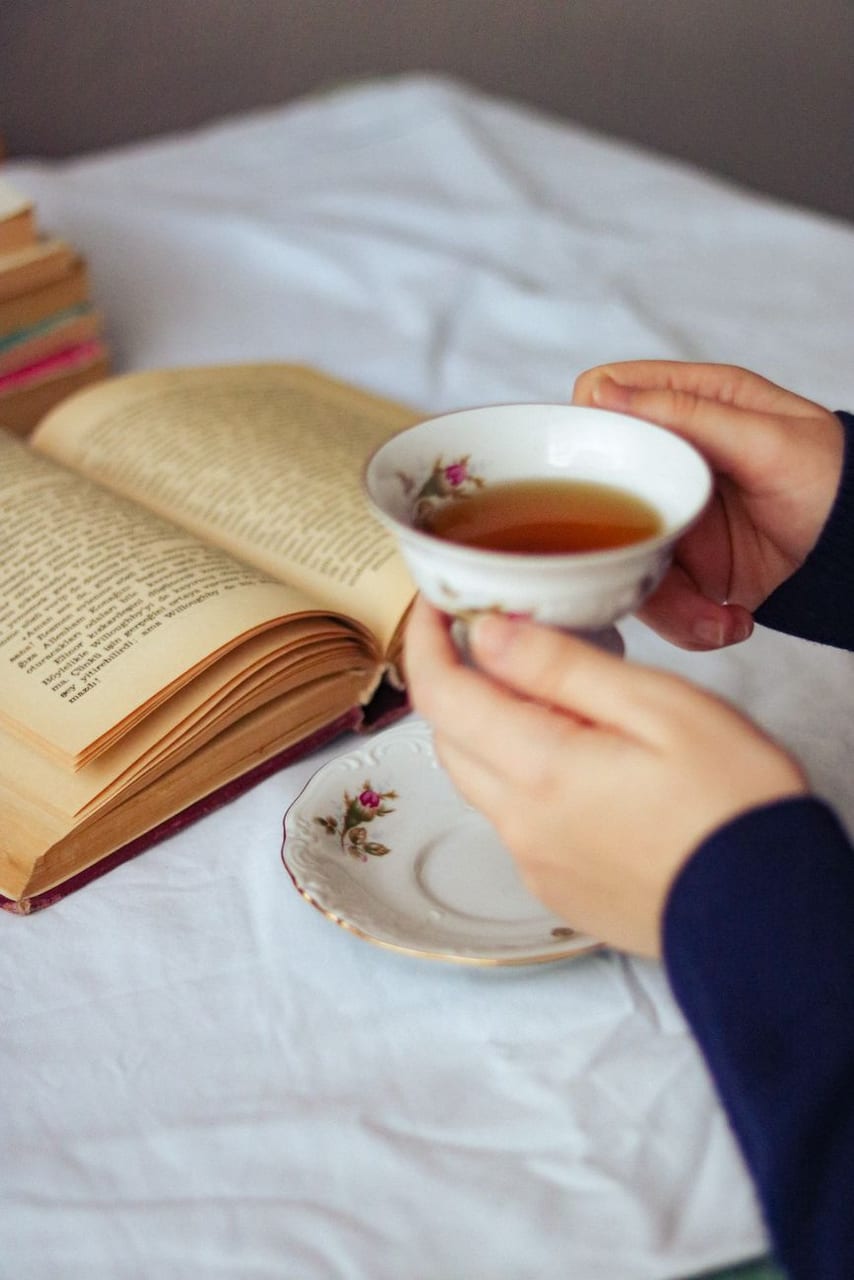 Hands holding a cup of tea over an open book